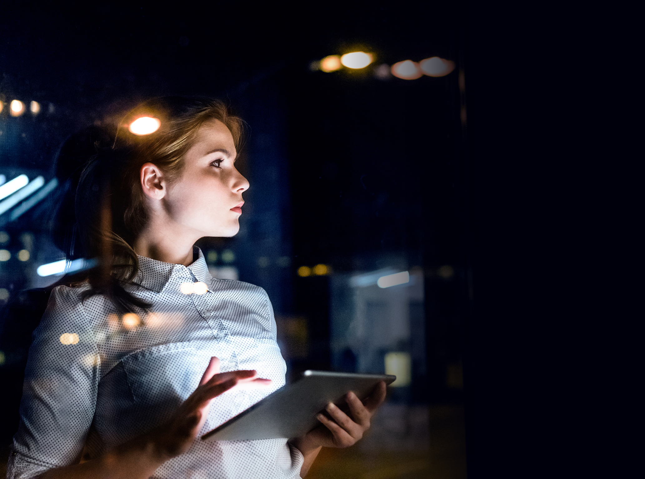 Beautiful young businesswoman with tablet in the office working late at night. Shot through glass.