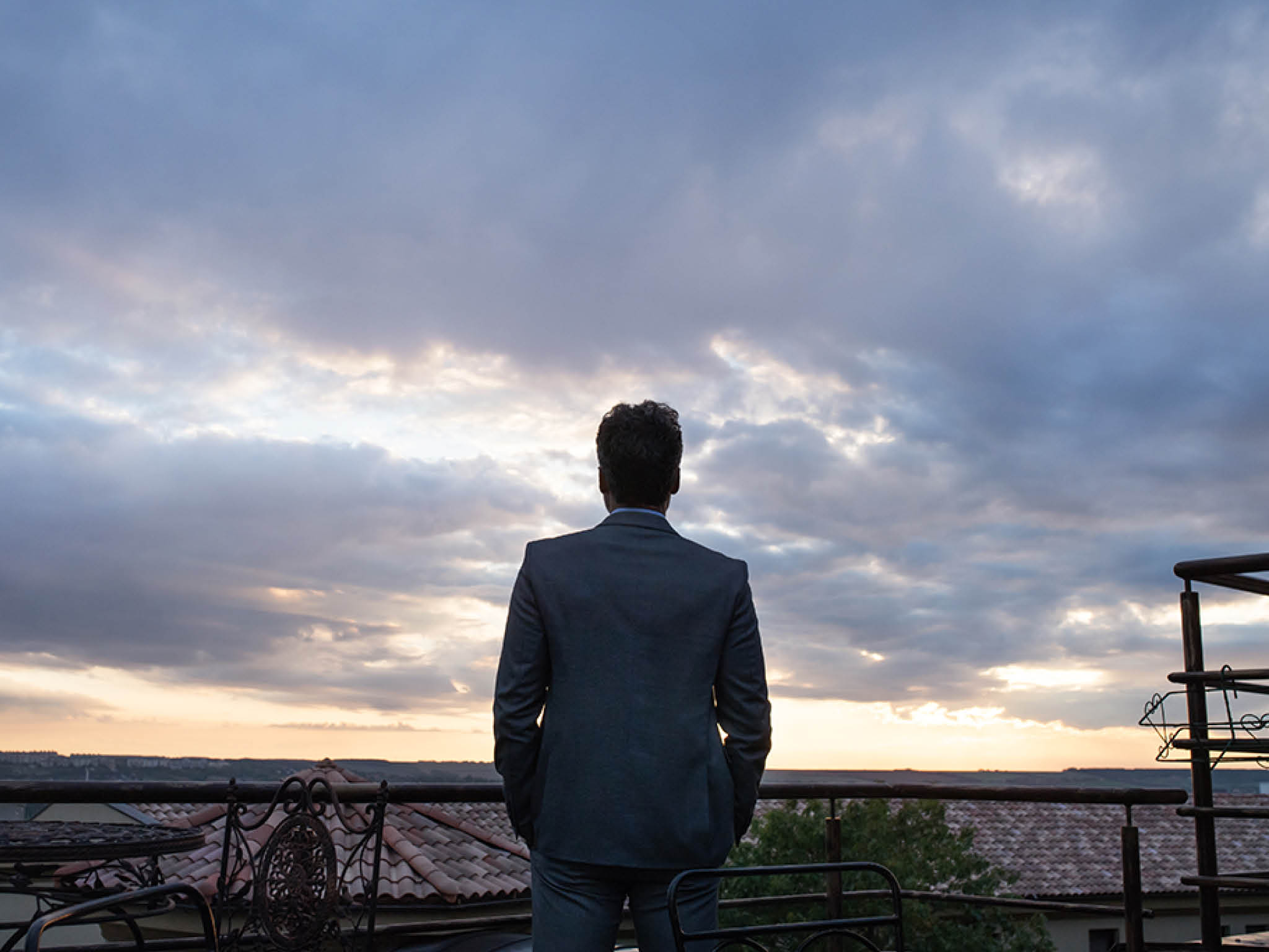 Mature businessman standing in a hotel balcony in the evening  Rear view 