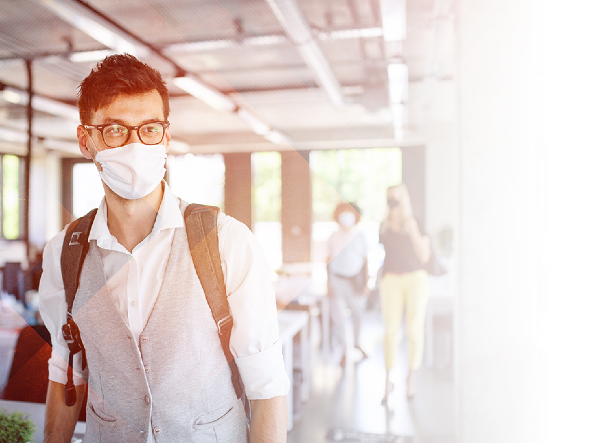 Portrait of young man with face mask back at work in office after lockdown, looking at camera 