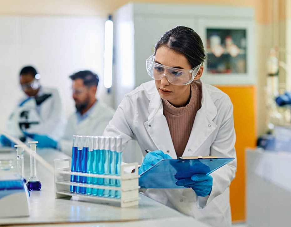 Female biochemist taking notes while examining liquid samples in test tubes during scientific research in a lab