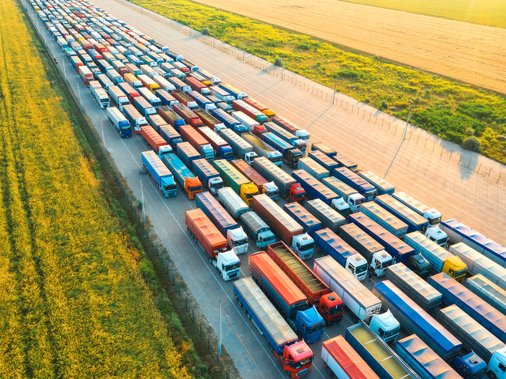 Aerial view of colorful trucks in terminal at sunset in summer. Top view of logistic center. Heavy industry. Transportation. Cargo transport, shipping. International trucking. View from drone of truck