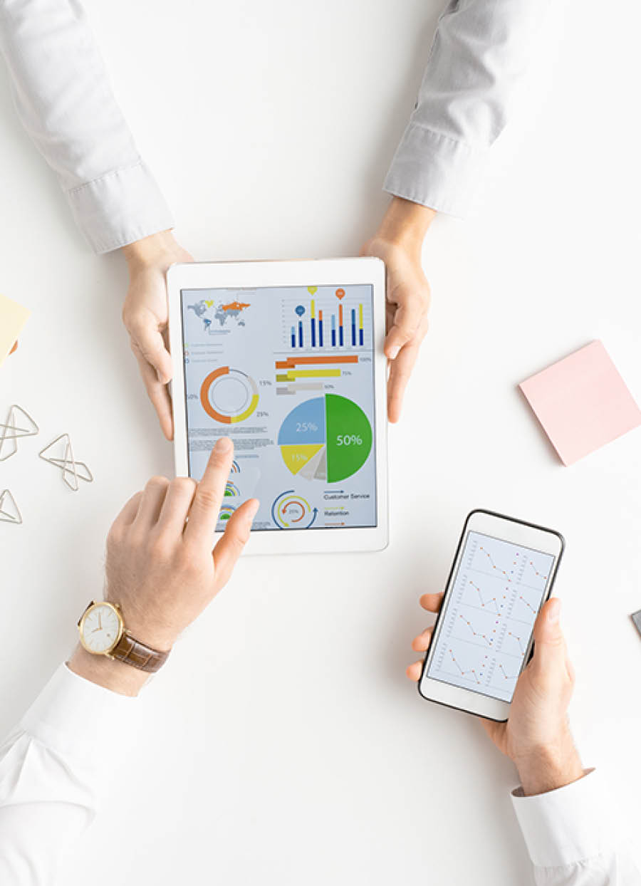 View of hands of two analysts or brokers with gadgets discussing financial data on touchscreen while one of them pointing at circle diagram