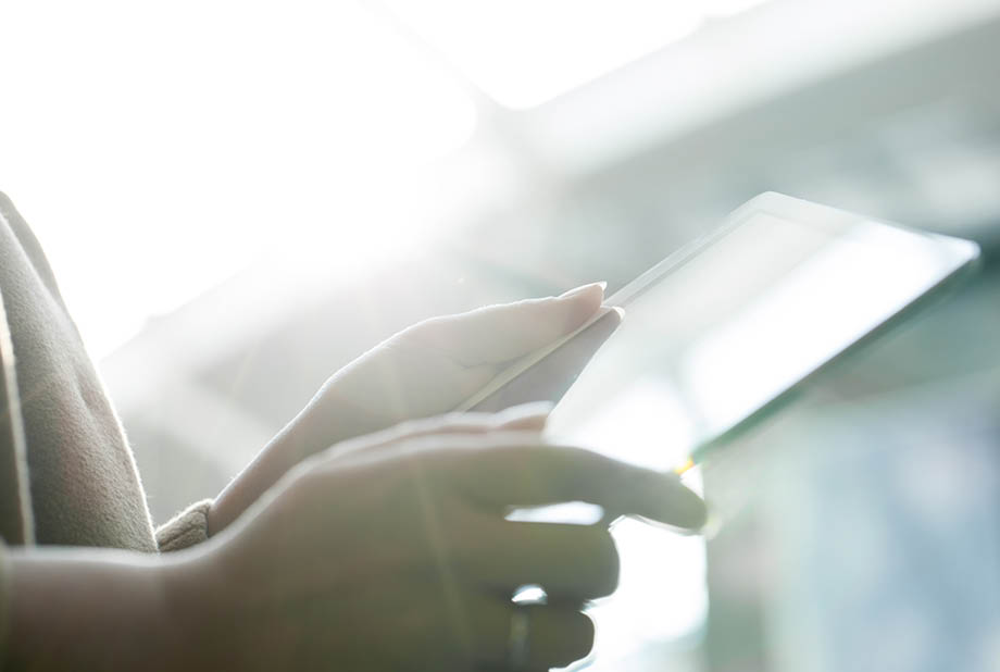 Close-up shot of female hands holding touch pad against bright sunlight